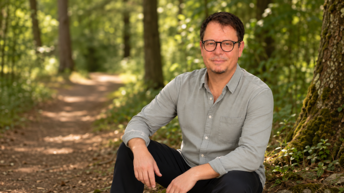 Tom Steiner – Zertifizierter PEMF-Praktiker für Regeneration und Achtsamkeit, entspannt sitzend im Wald als Zeichen für Ruhe und Entschleunigung.